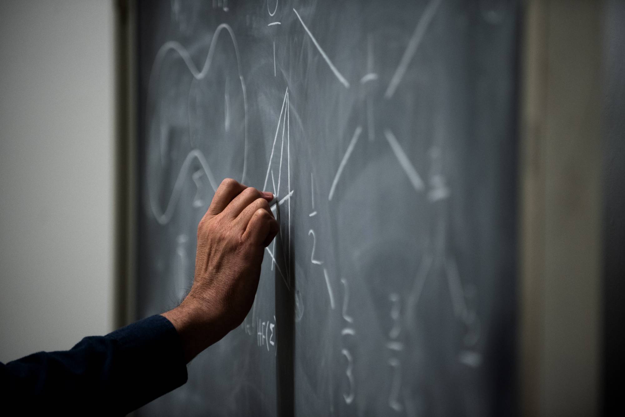 Someone's hand drawing equations on a chalk board